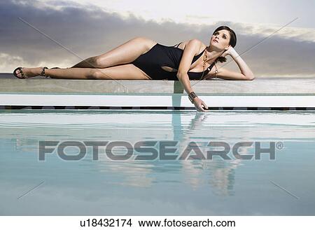 Picture - Woman in bathing suit reclining by pool. Fotosearch