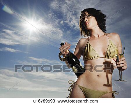 Stock Image - Woman in bikini holding champagne outdoors. Fotosearch