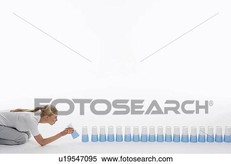 Stock Photography - Woman lining up plastic cups on ground against white background. Fotosearch