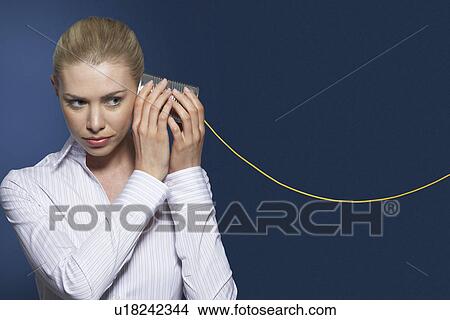 Woman listening to tin can phone against dark background View Large Photo Image Picture - Woman listening to tin can phone against dark background. Fotosearch
