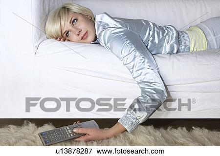 Woman lying on sofa holding remote control View Large Photo Image Stock Photo - Woman lying on sofa holding remote control. Fotosearch