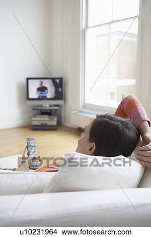 Woman lying on sofa watching television View Large Photo Image Picture - Woman lying on sofa watching television. Fotosearch