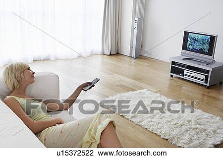 Woman lying on sofa watching television View Large Photo Image Stock Image - Woman lying on sofa watching television. Fotosearch
