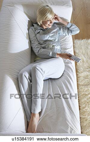 Stock Image - Woman lying on sofa watching television view from above. Fotosearch