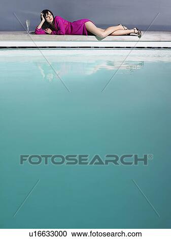 Stock Image - Woman reclining by pool with champagne glass. Fotosearch