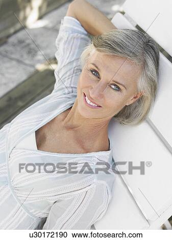 Stock Image - Woman reclining on sun lounger elevated view portrait. Fotosearch
