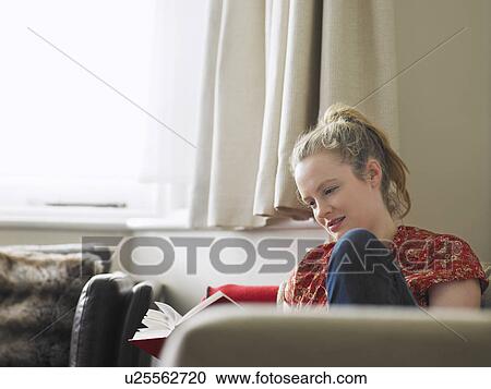 Stock Image - Woman sitting in living room reading book. Fotosearch