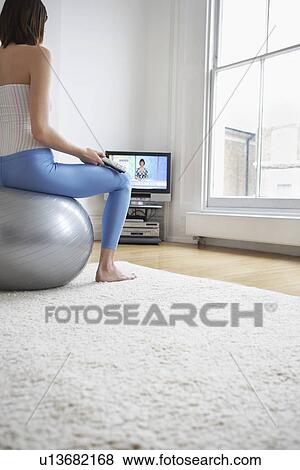 Stock Photo - Woman sitting on fitness ball watching television back view. Fotosearch