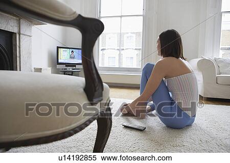 Stock Photography - Woman sitting on floor watching television back view. Fotosearch