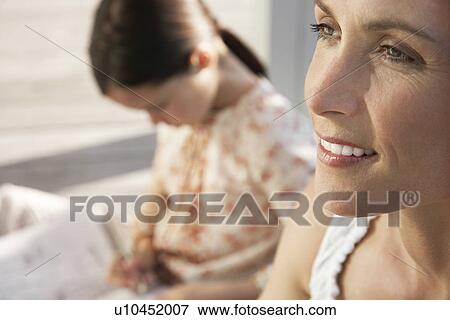 Stock Photo - Woman sitting on porch close up daughter in background. Fotosearch