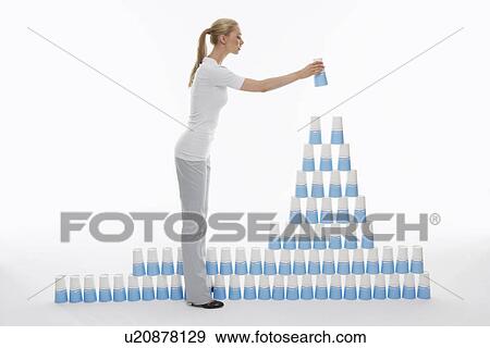 Stock Photo - Woman stacking plastic cups into pyramid against white background. Fotosearch