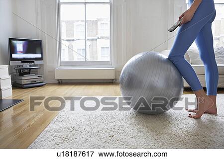 Stock Photo - Woman standing at fitness ball watching television low section. Fotosearch