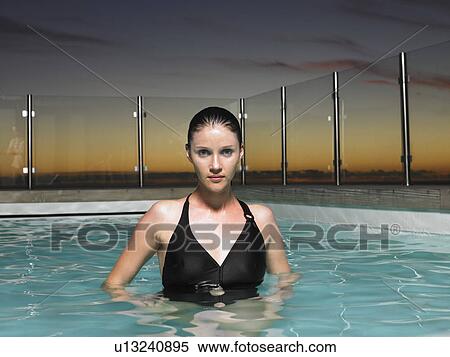 Stock Photography - Woman standing in outdoor swimming pool at sunset. Fotosearch