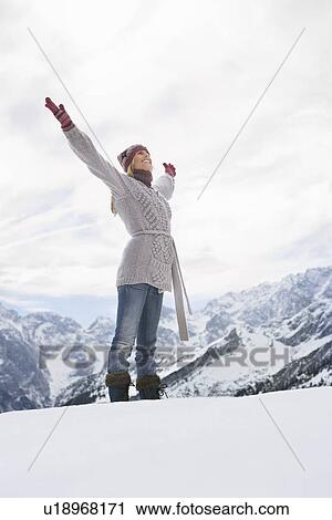 Stock Image - Woman standing on mountain peak with arms outstretched side view. Fotosearch