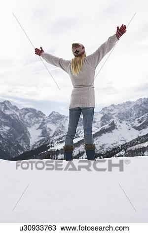 Stock Image - Woman standing on mountain peak with arms outstretched back view. Fotosearch