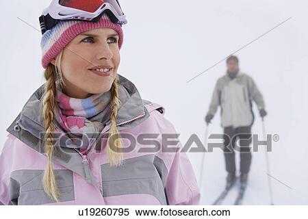Stock Photography - Woman standing on ski slope man on skis in background. Fotosearch