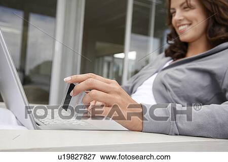 Stock Photo - Woman using laptop holding credit card sitting on porch. Fotosearch