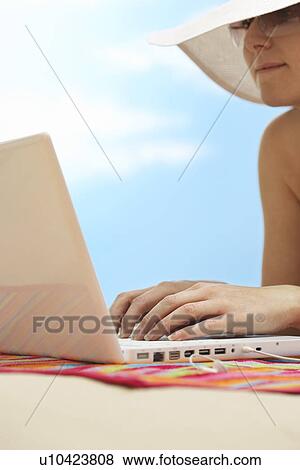 Stock Photo - Woman using laptop lying on stomach on beach close up. Fotosearch