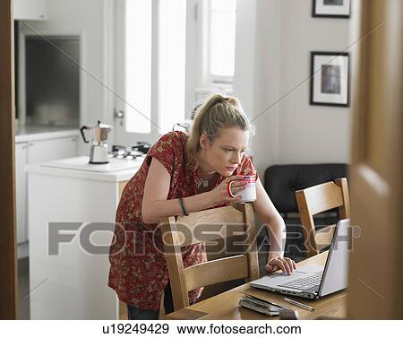 Stock Photo - Woman using laptop on dining table elevated view. Fotosearch