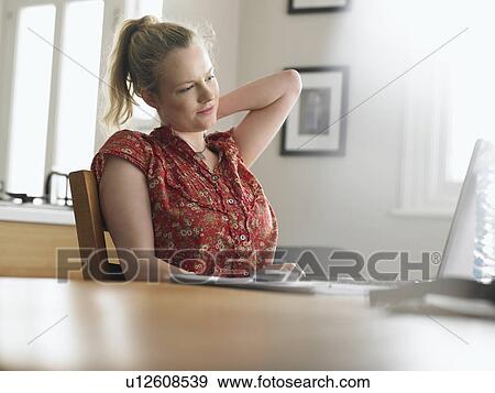 Woman using laptop sitting at dining table low angle view View Large Photo Image Stock Photo - Woman using laptop sitting at dining table low angle view. Fotosearch