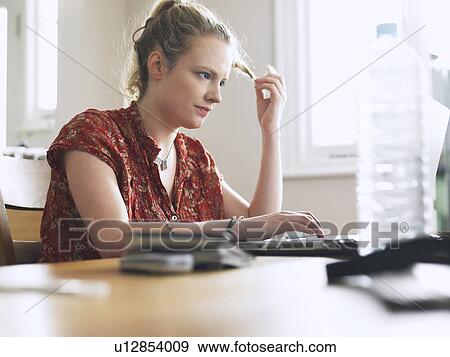 Woman using laptop sitting at dining table low angle view View Large Photo Image Stock Photo - Woman using laptop sitting at dining table low angle view. Fotosearch