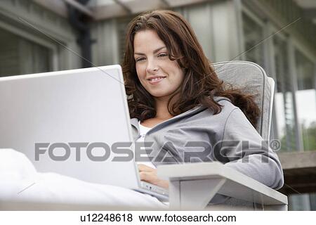 Woman using laptop sitting on porch half length View Large Photo Image Stock Photo - Woman using laptop sitting on porch half length. Fotosearch