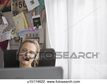 Woman using laptop wearing headset sitting at desk View Large Photo Image Stock Image - Woman using laptop wearing headset sitting at desk. Fotosearch