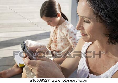 Woman using mobile phone sitting on porch with daughter reading book View Large Photo Image Stock Photo - Woman using mobile phone sitting on porch with daughter reading book. Fotosearch