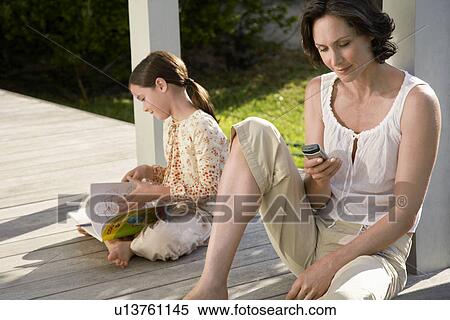 Woman using mobile phone sitting on porch with daughter reading book View Large Photo Image Stock Photography - Woman using mobile phone sitting on porch with daughter reading book. Fotosearch