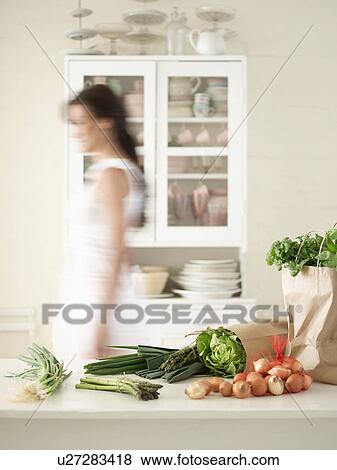 Stock Photo - Woman walking behind Fresh Produce on Kitchen Counter side view. Fotosearch