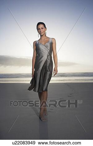 Stock Photo - Woman walking on beach at sunset low angle view portrait. Fotosearch