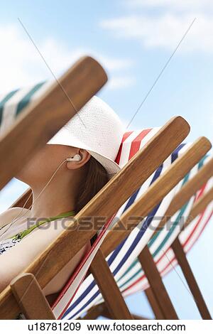 Woman wearing earphones sitting in deckchair side view View Large Photo Image Stock Photo - Woman wearing earphones sitting in deckchair side view. Fotosearch