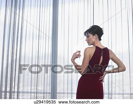 Stock Photography - Woman wearing elegant dress looking out of window indoors. Fotosearch