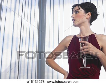 Stock Image - Woman wearing elegant dress with champagne in front of window. Fotosearch