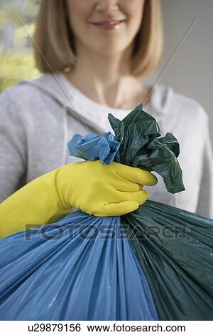 Stock Photograph - Woman wearing rubber gloves holding garbage bag close-up. Fotosearch