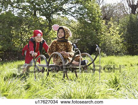 Picture - Young boy (7-9) in pirate costume pushing boy (5-6) in cart in jaguar costume smiling. Fotosearch