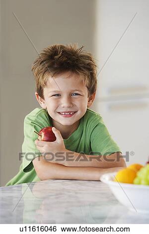Young boy holding apple in kitchen View Large Photo Image Stock Photograph - Young boy holding apple in kitchen. Fotosearch