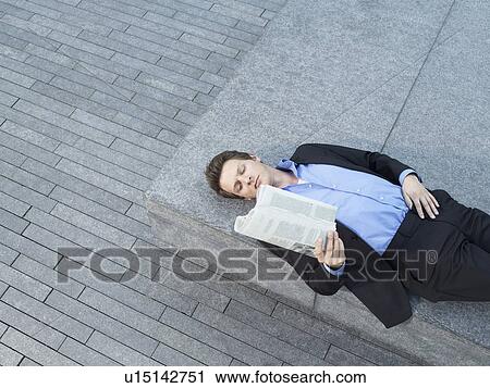 Young businessman lying on wall on pavement reading newspaper elevated view View Large Photo Image Stock Image - Young businessman lying on wall on pavement reading newspaper elevated view. Fotosearch