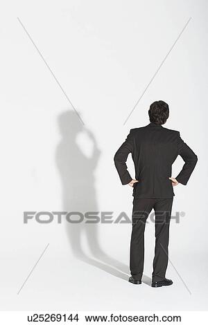 Young businessman standing hands on hip arguing with own shadow back view View Large Photo Image Picture - Young businessman standing hands on hip arguing with own shadow back view. Fotosearch