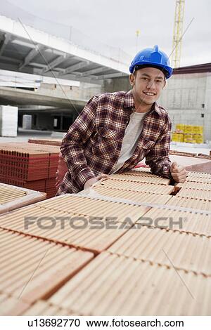 Stock Image - Young construction worker leaning on tiles. Fotosearch