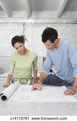 Stock Image - Young couple at desk man pointing at blueprint. Fotosearch