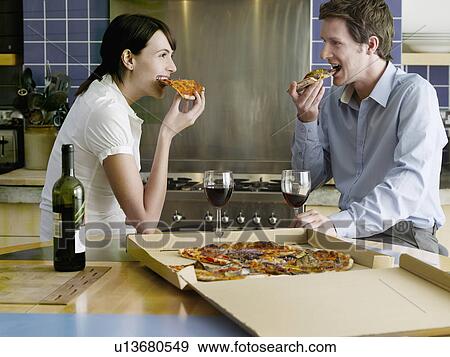 Young couple eating pizza in kitchen View Large Photo Image Stock Photo - Young couple eating pizza in kitchen. Fotosearch
