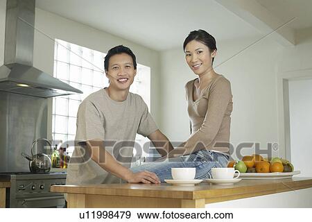 Stock Photo - Young Couple husband standing wife sitting on bar in Kitchen portrait. Fotosearch