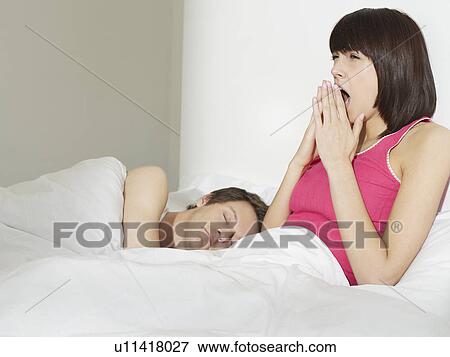 Young couple in bed man sleeping woman yawning View Large Photo Image Stock Photo - Young couple in bed man sleeping woman yawning. Fotosearch
