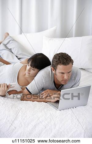 Young couple lying on bed man using laptop woman reading View Large Photo Image Stock Photography - Young couple lying on bed man using laptop woman reading. Fotosearch