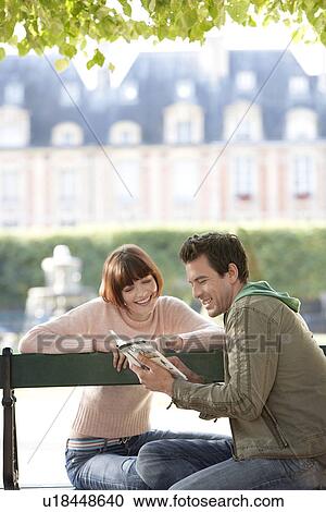 Young couple reading guide book sitting on bench in park View Large Photo Image Stock Image - Young couple reading guide book sitting on bench in park. Fotosearch