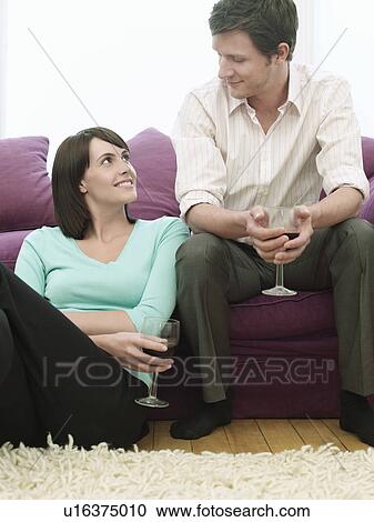 Stock Image - Young couple relaxing on sofa drinking wine. Fotosearch