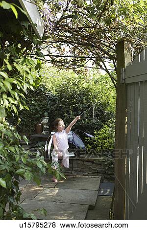 Stock Photo - Young girl (5-6) sitting in garden in fairy costume holding magic wand. Fotosearch