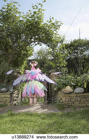 Young girl (5-6) wearing fairy costume standing in garden back view View Large Photo Image Picture - Young girl (5-6) wearing fairy costume standing in garden back view. Fotosearch