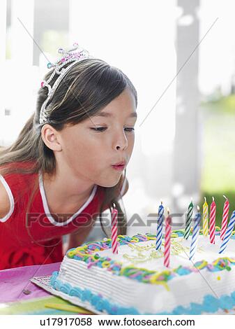 Stock Photo - Young girl (7-9) blowing out birthday candles close-up. Fotosearch
